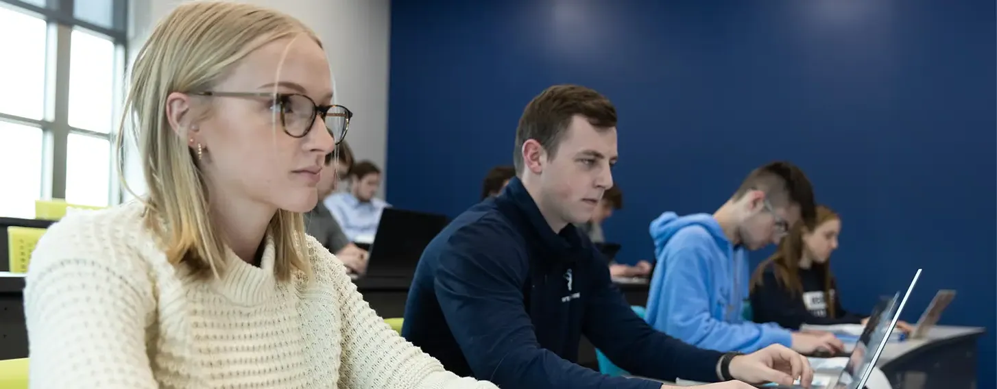 Students in a classroom sitting at desks, focused on laptops.