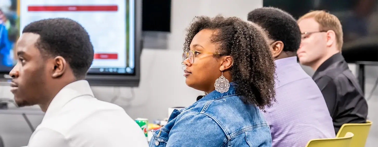 A woman sitting in a classroom alongside other students looking across the room.